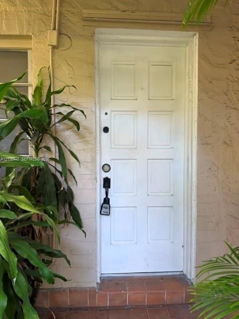 Eight-panel white entry door set within a textured stucco exterior wall, featuring a tiled threshold and traditional hardware