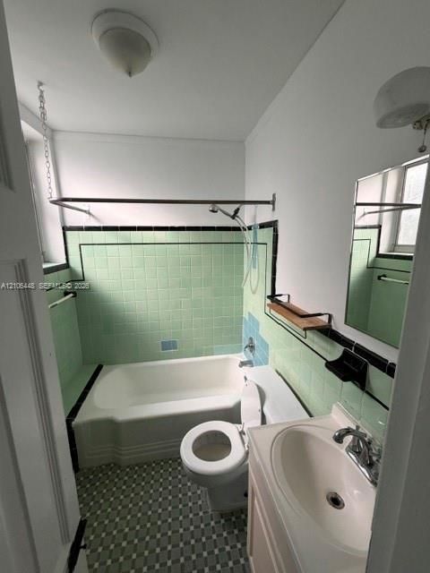 Bathroom featuring a porcelain tub with integrated tile surround, pedestal sink, geometric patterned floor tiling, and wall-mounted vanity mirror