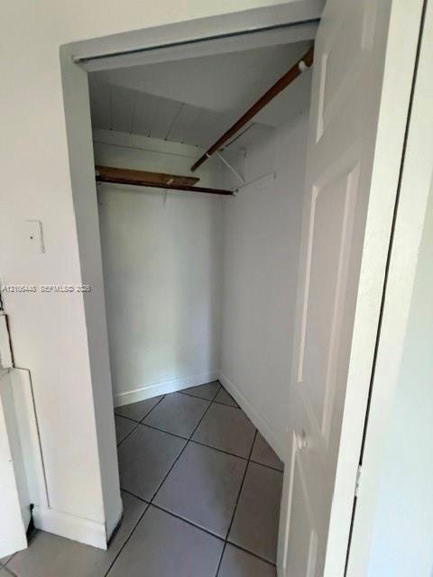 Storage closet featuring neutral floor tile, a built-in shelf, and a hanging rod