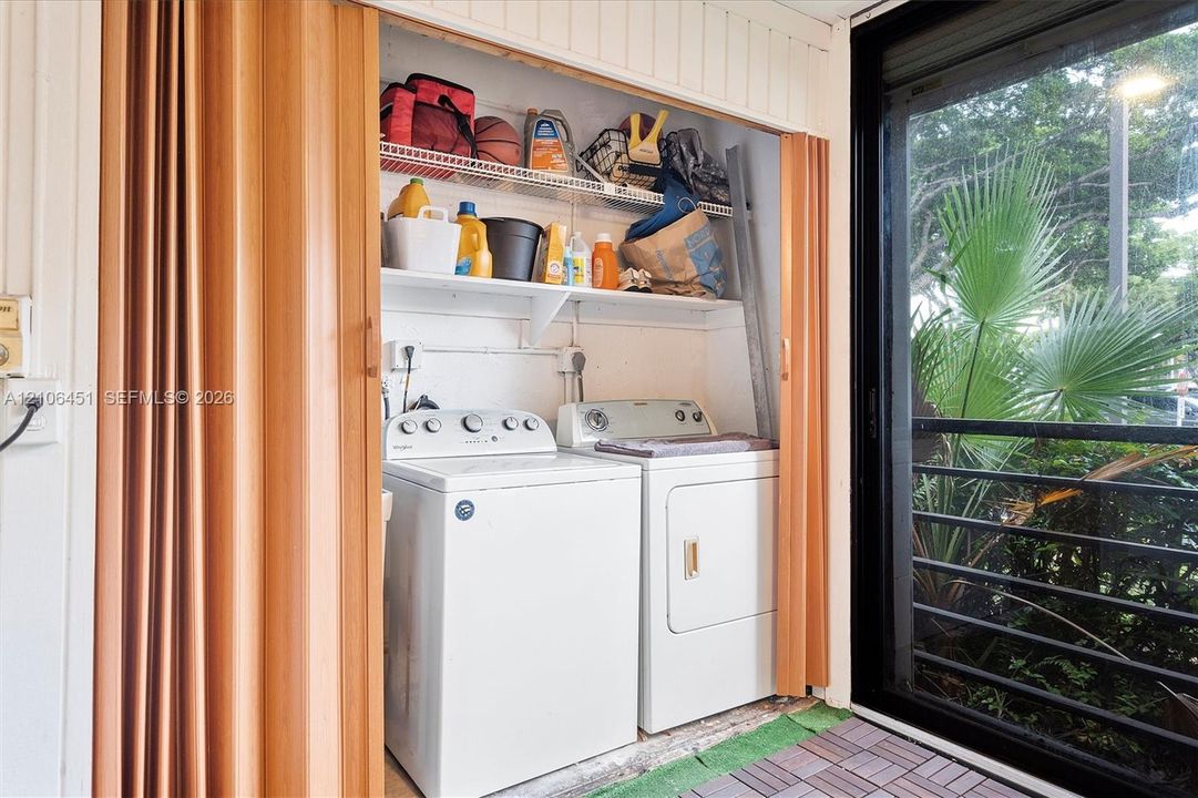 Laundry area featuring folding accordion doors, two integrated wire storage shelves, and sliding glass exterior doors with metal railing
