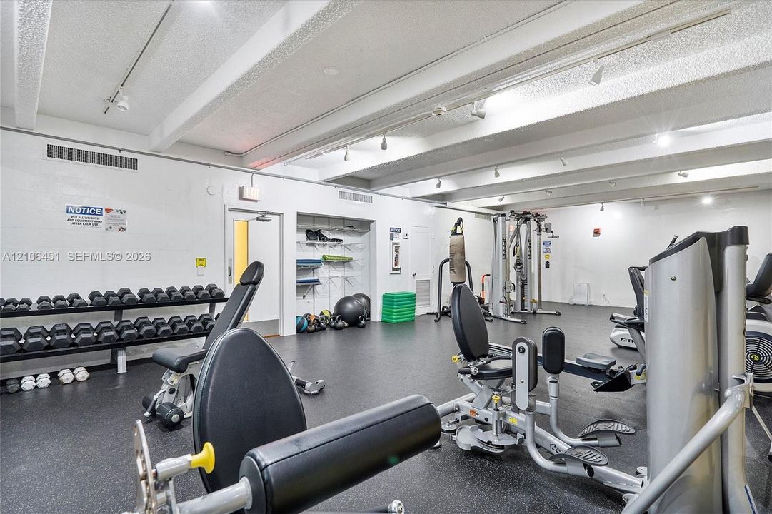 Fitness center featuring industrial-style exposed ceiling beams, track lighting, rubberized flooring, and built-in recessed shelving