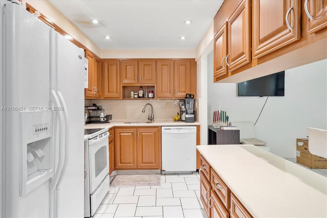 Kitchen featuring medium-tone wood cabinetry, white tile flooring, white appliances, solid-surface countertops, and recessed ceiling lighting