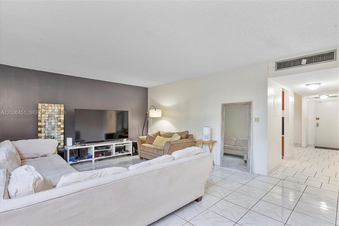 Open-concept interior featuring light-toned tile flooring, a charcoal-painted accent wall, and a recessed ceiling-mounted climate control system
