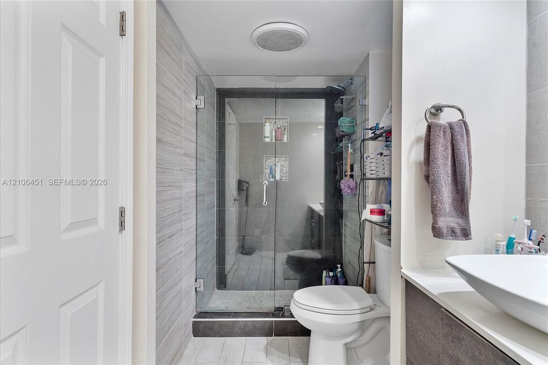 Bathroom featuring a walk-in shower with glass enclosure, recessed shower niche, vessel sink, and textured tile wall accents