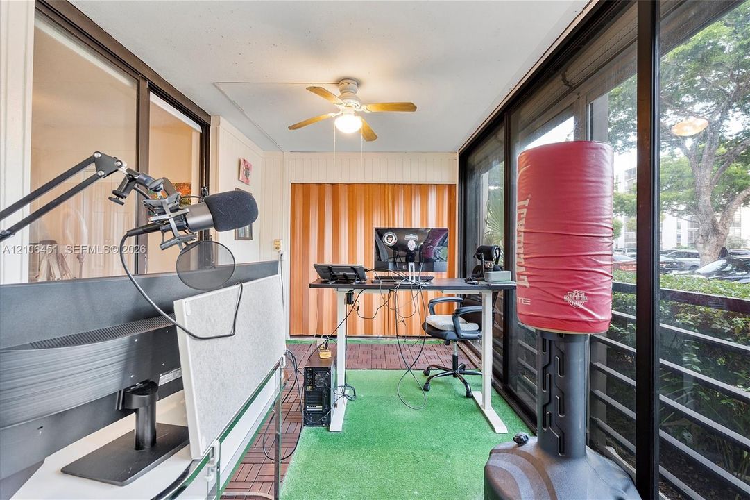 Enclosed sunroom featuring floor-to-ceiling sliding glass panels, vertical wood-panel accent wall, and a ceiling-mounted light fixture with fan