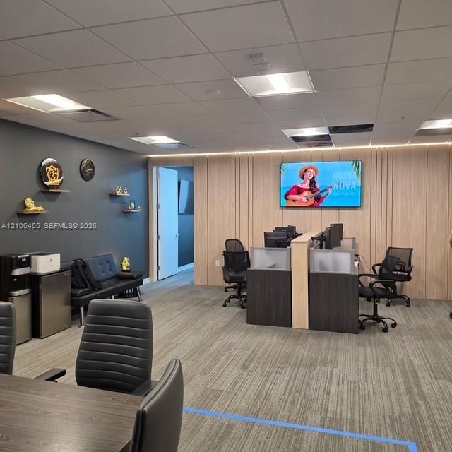 Office space featuring drop ceiling with recessed lighting, integrated wood-slat accent wall, and patterned carpeted flooring