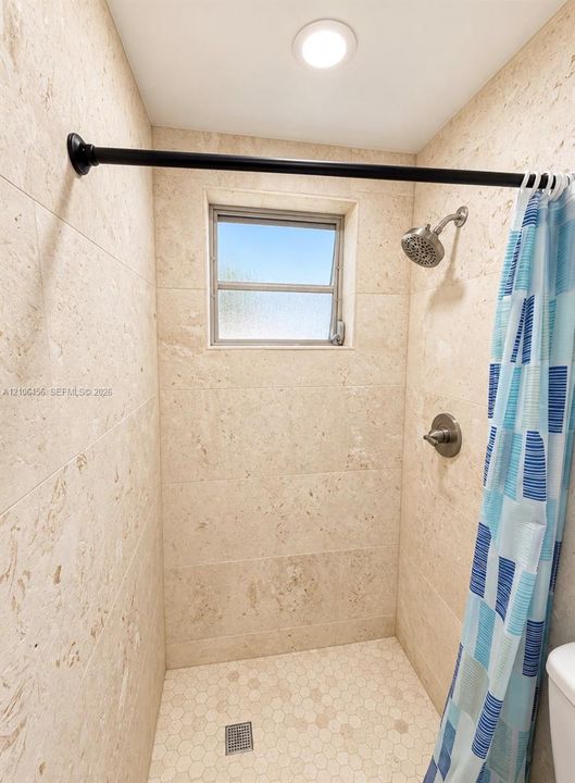 Shower stall featuring floor-to-ceiling stone-finish tile walls, hexagonal floor tile, a recessed window, and a wall-mounted shower head