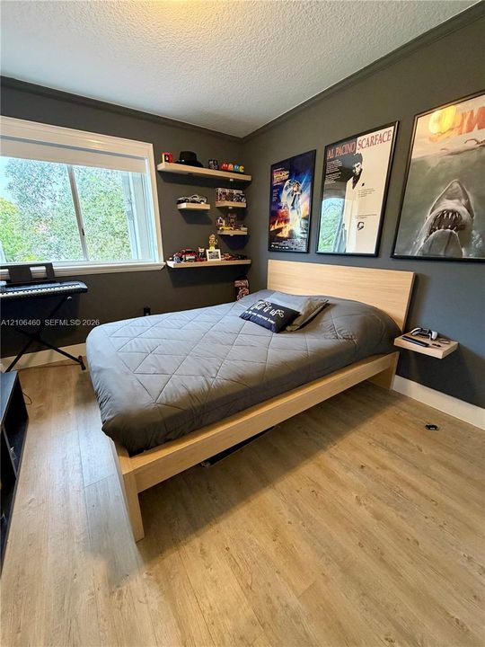 Wood-finish flooring, large window with neutral trim, charcoal-toned walls, and multiple wall-mounted floating wood shelves