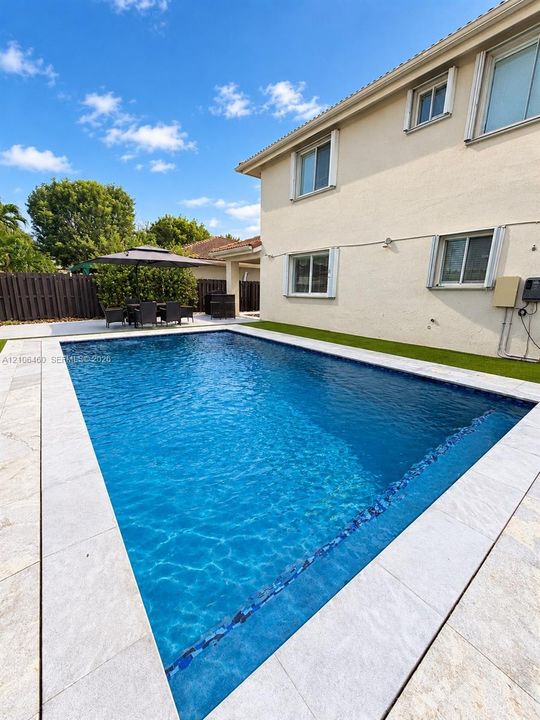 Rectangular in-ground swimming pool with blue tile inlay and light-toned stone pool decking