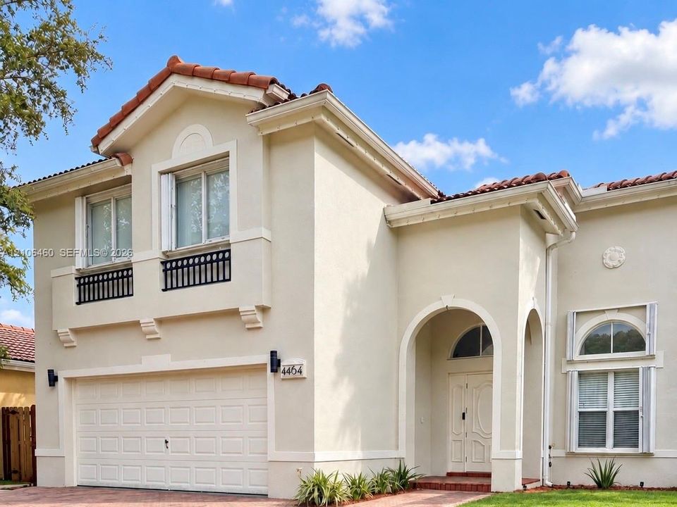 Stucco exterior featuring a clay tile roof, arched entryway, upper-level decorative railing, and a multi-panel garage door