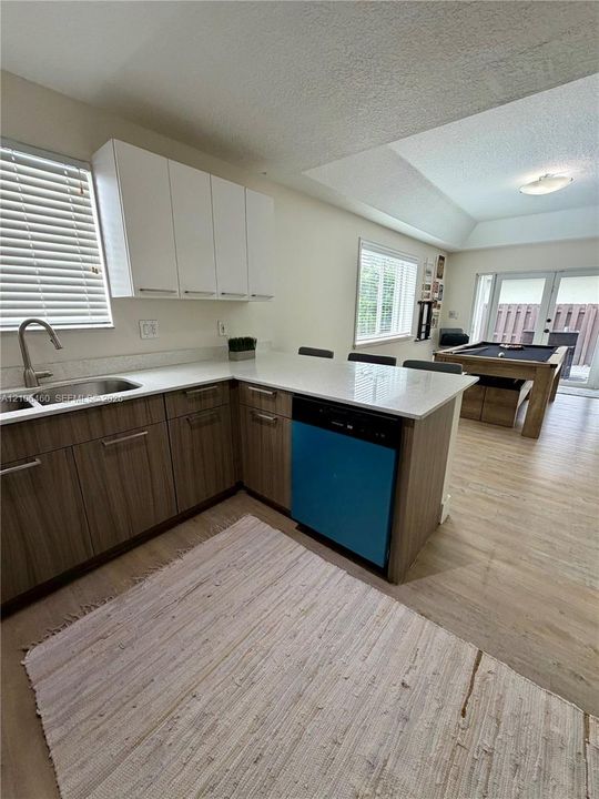 Kitchen featuring a dual-tone cabinet palette, quartz countertops, undermount stainless steel sink with gooseneck faucet, and wood-finish flooring