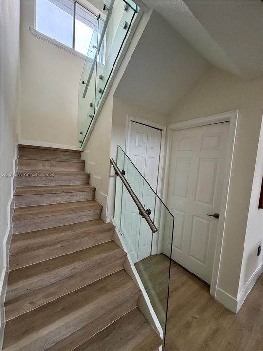 Staircase featuring wood-finish flooring, glass panel railings, and metal handrail