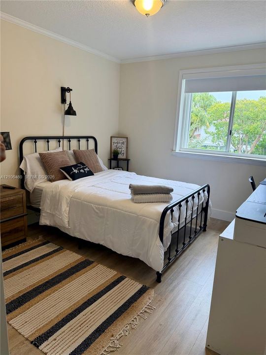 Neutral interior space featuring wood-finish flooring, a wall-mounted industrial-style light fixture, and a single-hung window with exterior greenery