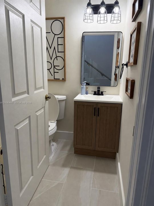 Bathroom featuring a wood-tone vanity, white countertop with an integrated sink, matte black hardware, rectangular mirror with rounded corners, and tile flooring