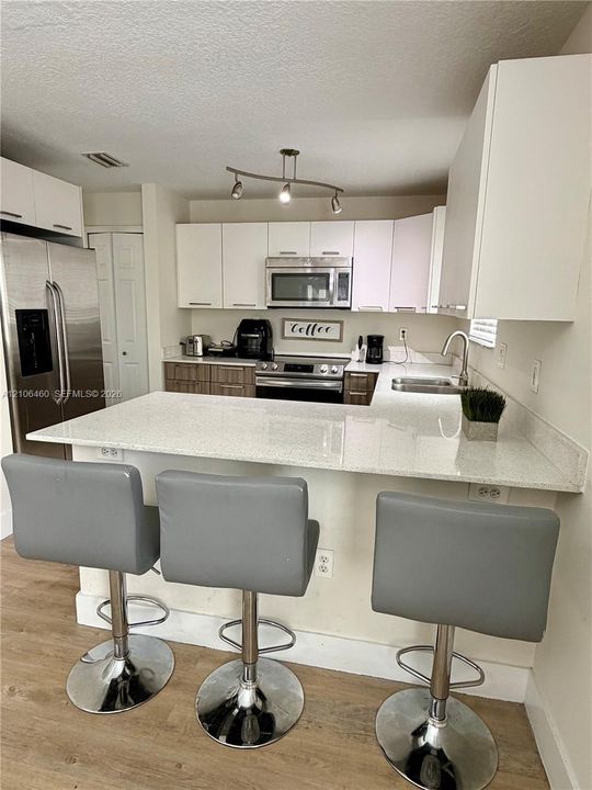 Kitchen featuring a peninsula with a stone-finish countertop, dual-tone cabinetry, stainless steel appliances, and track lighting