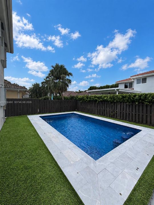 Backyard featuring an in-ground pool with stone-style coping, synthetic turf lawn, and a vertical wood-plank privacy fence