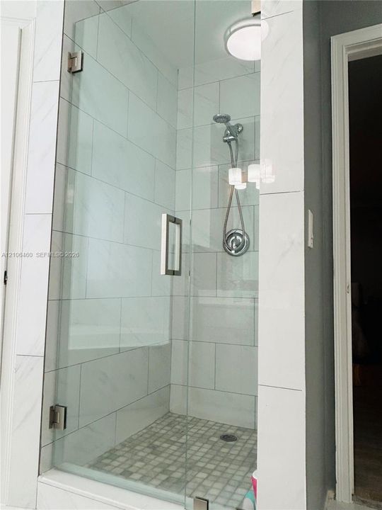 Walk-in shower featuring a frameless glass door, large-format tile wall surround, mosaic tile flooring, and a chrome handheld shower fixture