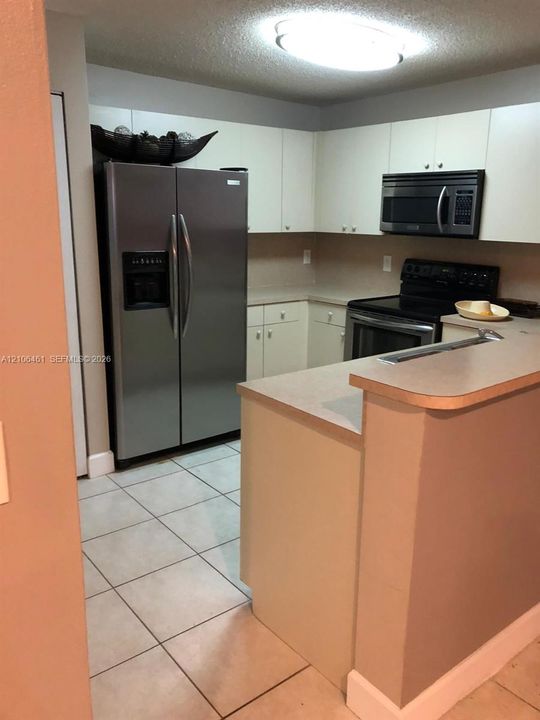 Kitchen featuring solid-surface countertops, flat-panel cabinetry, a stainless steel side-by-side refrigerator, a built-in microwave, and tile flooring