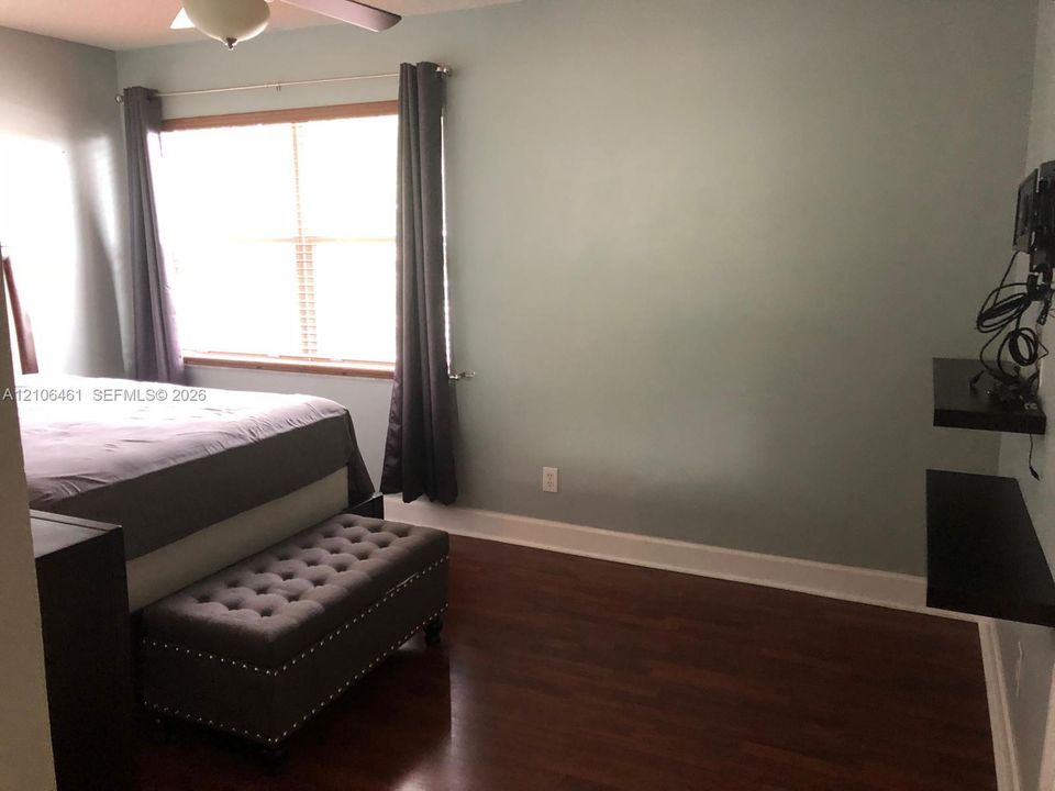 Bedroom featuring wood-finish flooring, a large window, built-in wall-mounted shelving, and a ceiling fan with light fixture