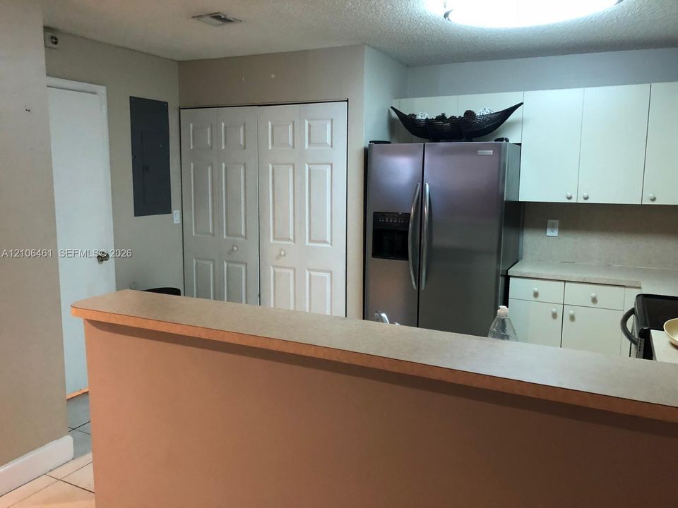 Kitchen featuring flat-panel cabinetry, a stainless steel refrigerator, neutral solid-surface countertops, and a breakfast bar