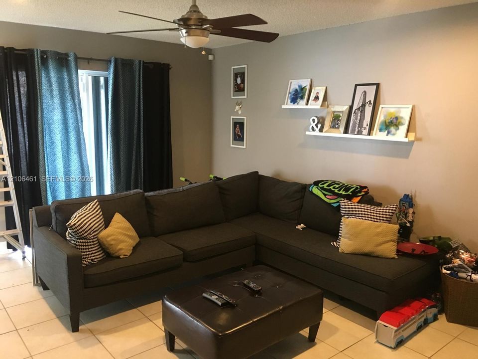 Neutral-toned interior space featuring large-format tile flooring, a mounted floating wall ledge, and a ceiling-mounted light fixture with a multi-blade fan