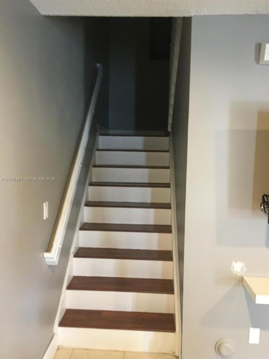 Staircase featuring wood-finish treads, painted risers, and a continuous wall-mounted handrail