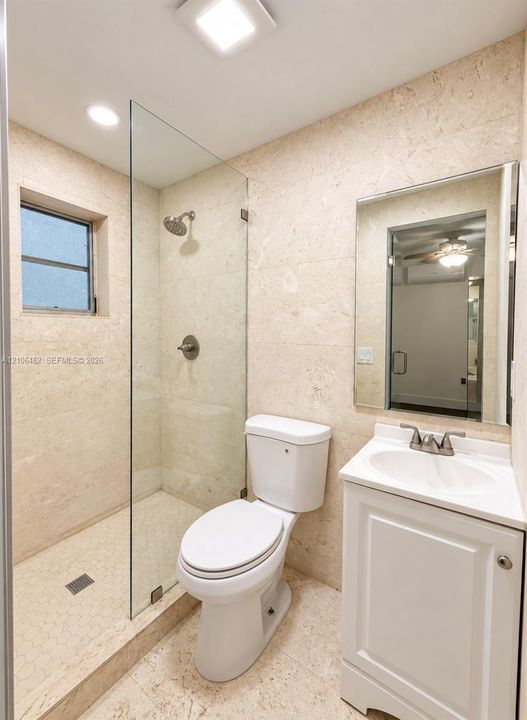 Full-height stone wall tiling, glass-enclosed walk-in shower with integrated stone floor, white pedestal-style vanity with built-in sink, and wall-mounted vanity mirror