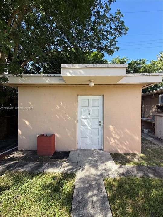 Detached structure featuring a flat roofline, smooth stucco exterior, and a central paneled entry door with a dedicated overhead exterior light fixture