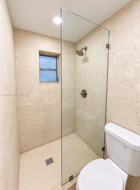 Walk-in shower featuring floor-to-ceiling stone wall tiling, a frameless glass enclosure, a mosaic tile shower floor, and a metal rainfall showerhead