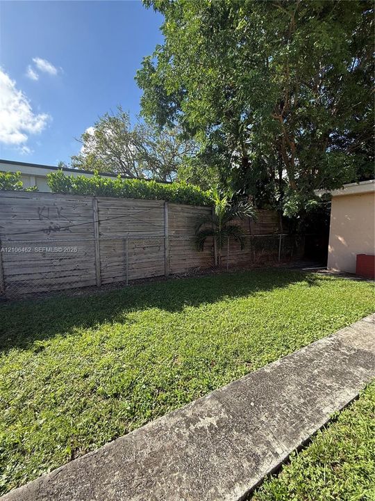 Backyard featuring a grass lawn, concrete walkway, horizontal wood privacy fencing, and mature trees