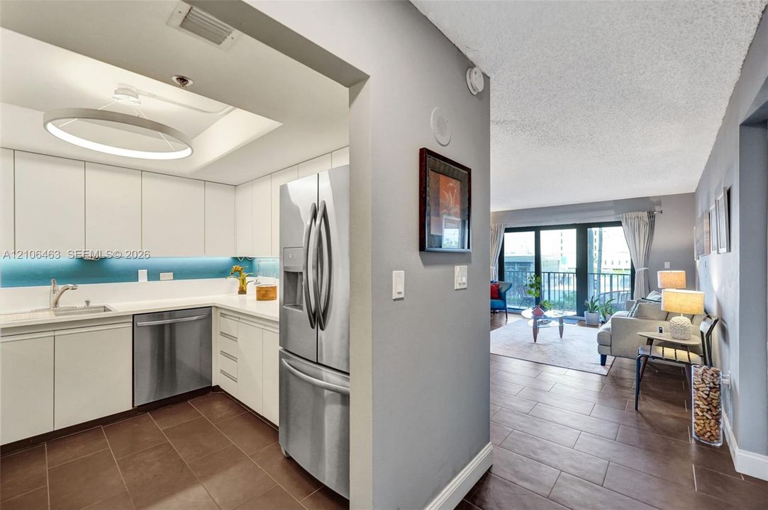 Kitchen featuring white flat-panel cabinetry, stainless steel refrigerator and dishwasher, recessed ceiling lighting, circular pendant fixture, and large-format tile flooring