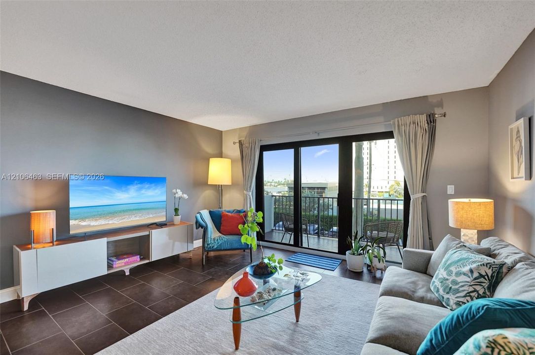 Living area featuring large format tile flooring, a dark-toned accent wall, and sliding glass doors with metal framing opening to a balcony