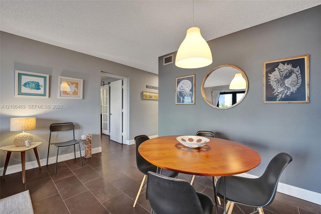 Neutral-toned walls featuring a recessed-mount round mirror, complemented by dark ceramic tile flooring and a minimalist dome-style pendant lighting fixture