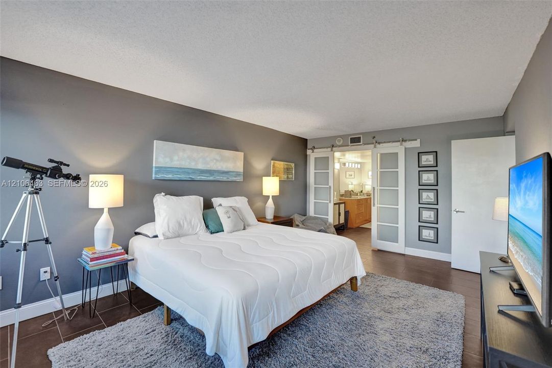 Spacious room featuring dark-toned walls, tile flooring, and dual glass-panel sliding barn doors with stainless steel hardware