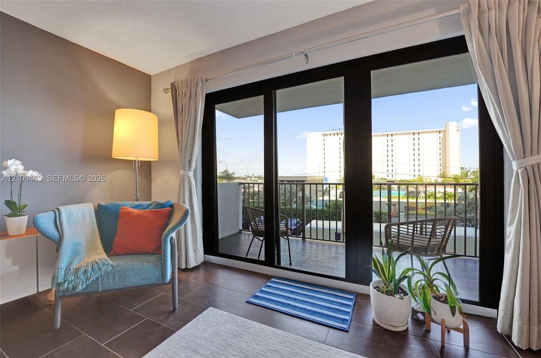 Large black-framed sliding glass doors opening to a private balcony with metal railings and tile flooring