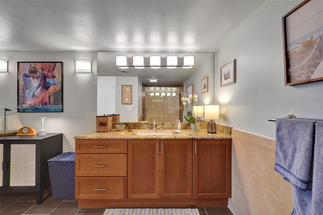 Wood-finish vanity cabinetry with an integrated countertop, large wall-mounted vanity mirror, five-light fixture, and ceramic tile wainscoting