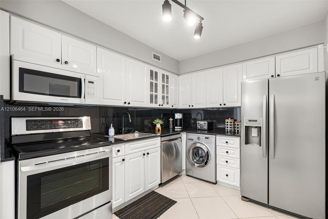 Kitchen featuring white shaker-style cabinetry, high-contrast dark stone countertops, stainless steel appliances, built-in front-load laundry, and tile flooring