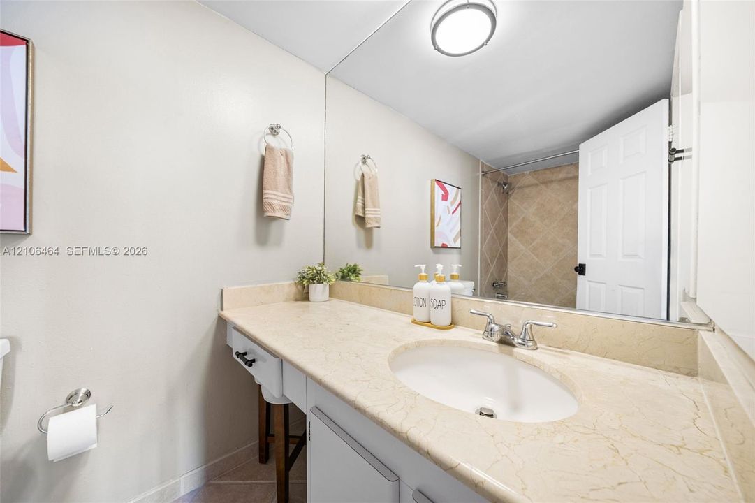 Bathroom featuring a vanity with a stone countertop, oval undermount sink, full-width wall mirror, and a tiled shower surround