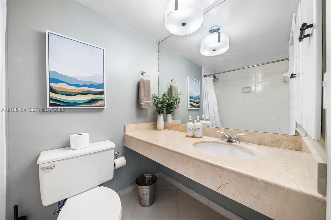 Wall-to-wall vanity with integrated stone-finish countertop, undermount oval sink, chrome dual-handle faucet, large-scale vanity mirror, and dual drum-style light fixtures