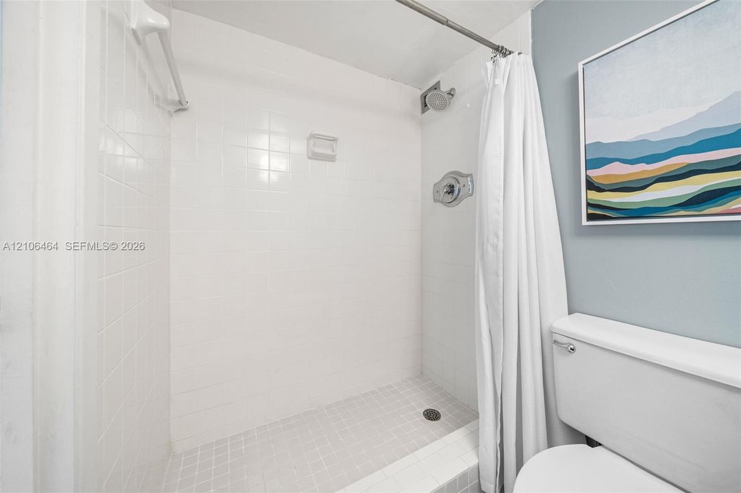 Shower alcove featuring floor-to-ceiling square tile surround, built-in soap niche, and wall-mounted shower head