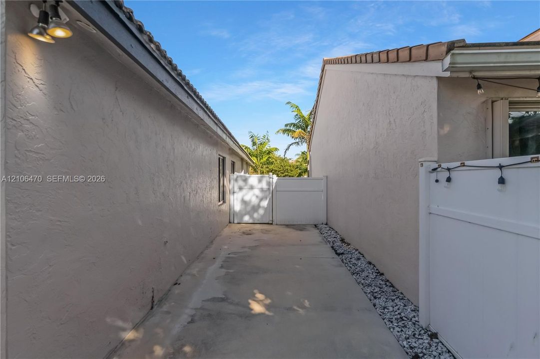 Exterior side yard featuring stucco walls, a concrete walkway, decorative stone border, and a privacy gate