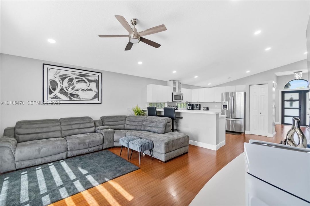 Open-concept interior featuring wood-finish flooring, white cabinetry, stainless steel appliances, recessed lighting, and a vaulted ceiling with a central brushed-metal ceiling fan