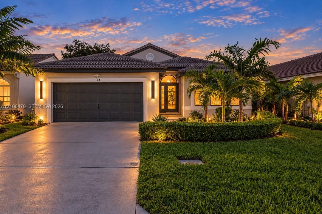 Single-story residence featuring a tile roof, concrete driveway, attached multi-car garage, manicured landscaping, and exterior wall-mounted lighting
