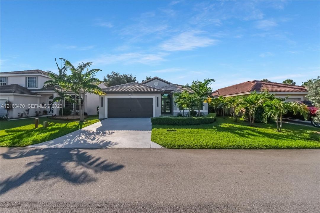 Single-story exterior featuring a concrete tile roof, stucco facade, two-car garage, and manicured landscaping