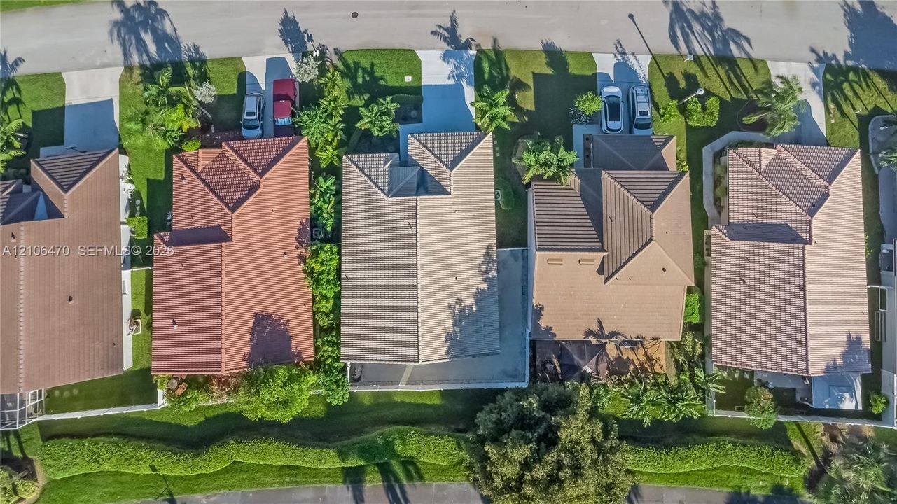 Aerial perspective featuring a residential lot with a concrete driveway, multi-hipped roofline, and landscaped backyard greenery