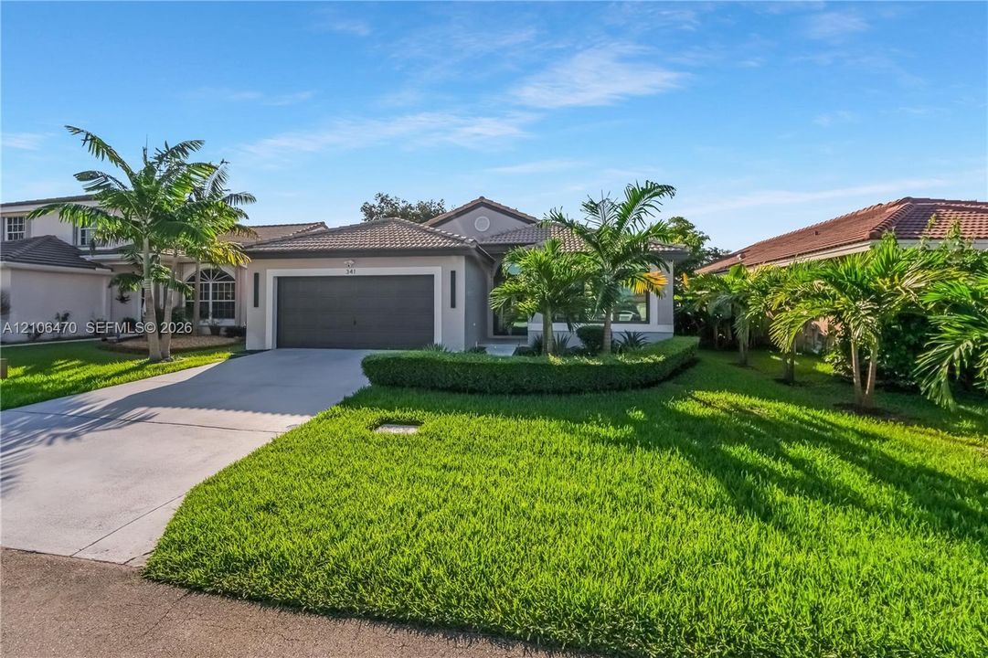 Single-story residence featuring a concrete tile roof, stucco exterior, two-car garage, concrete driveway, and professional landscaping with palm trees