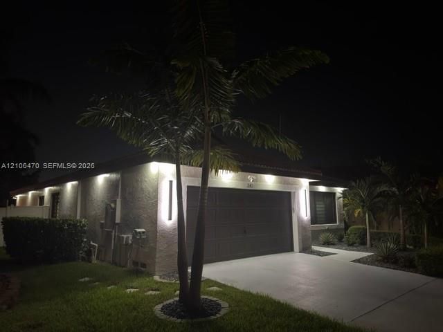Exterior facade featuring stucco siding, a multi-car garage, recessed soffit lighting, vertical wall-mounted exterior light fixtures, and palm tree landscaping