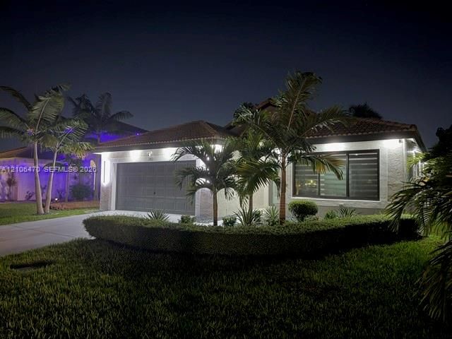 Single-story residence featuring a textured stucco exterior, tile roofing, an integrated two-car garage, and manicured landscaping with mature palms