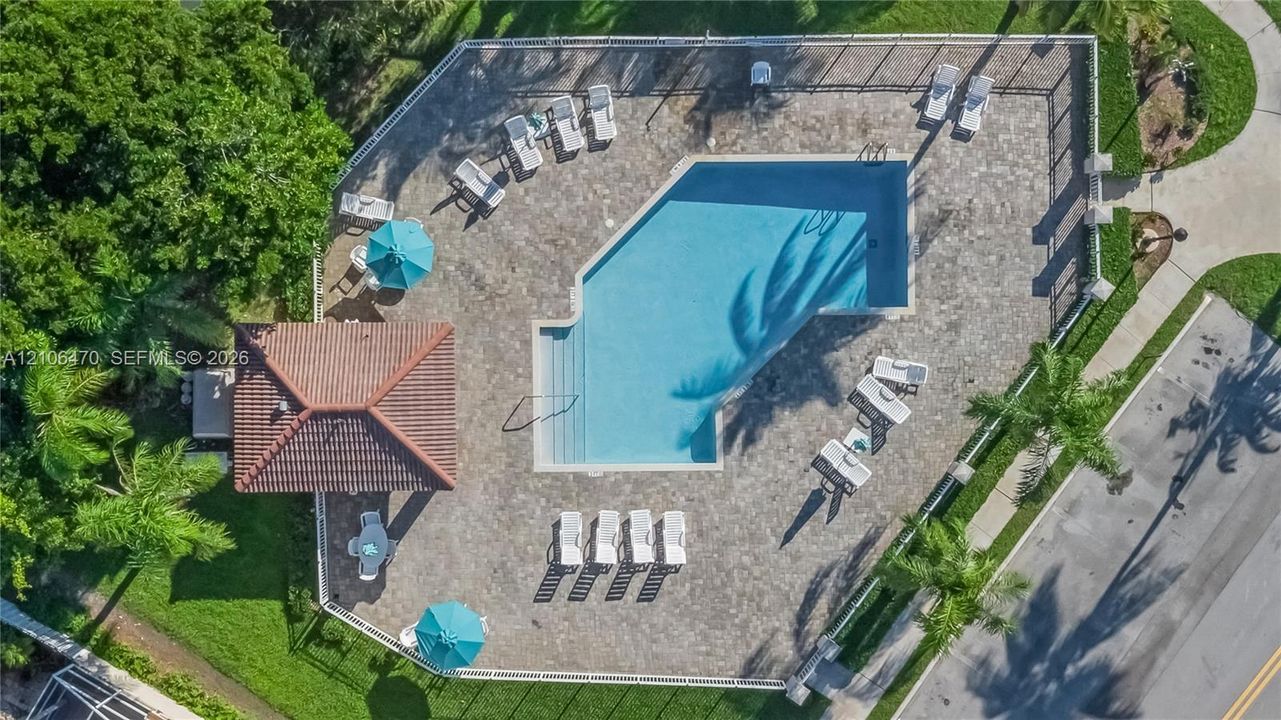 Swimming pool with a stone paver deck, covered cabana with a tile roof, perimeter fencing, and surrounding mature landscaping
