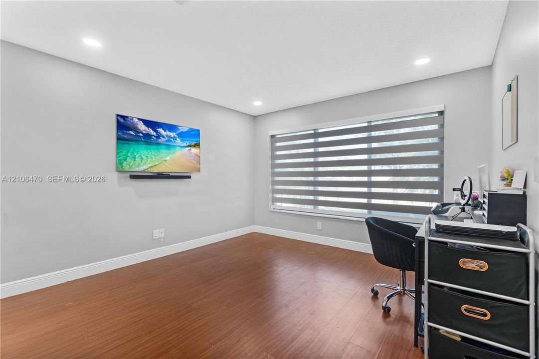 Neutral interior room featuring wood-finish flooring, recessed lighting, and a large window equipped with dual-layered roller shades